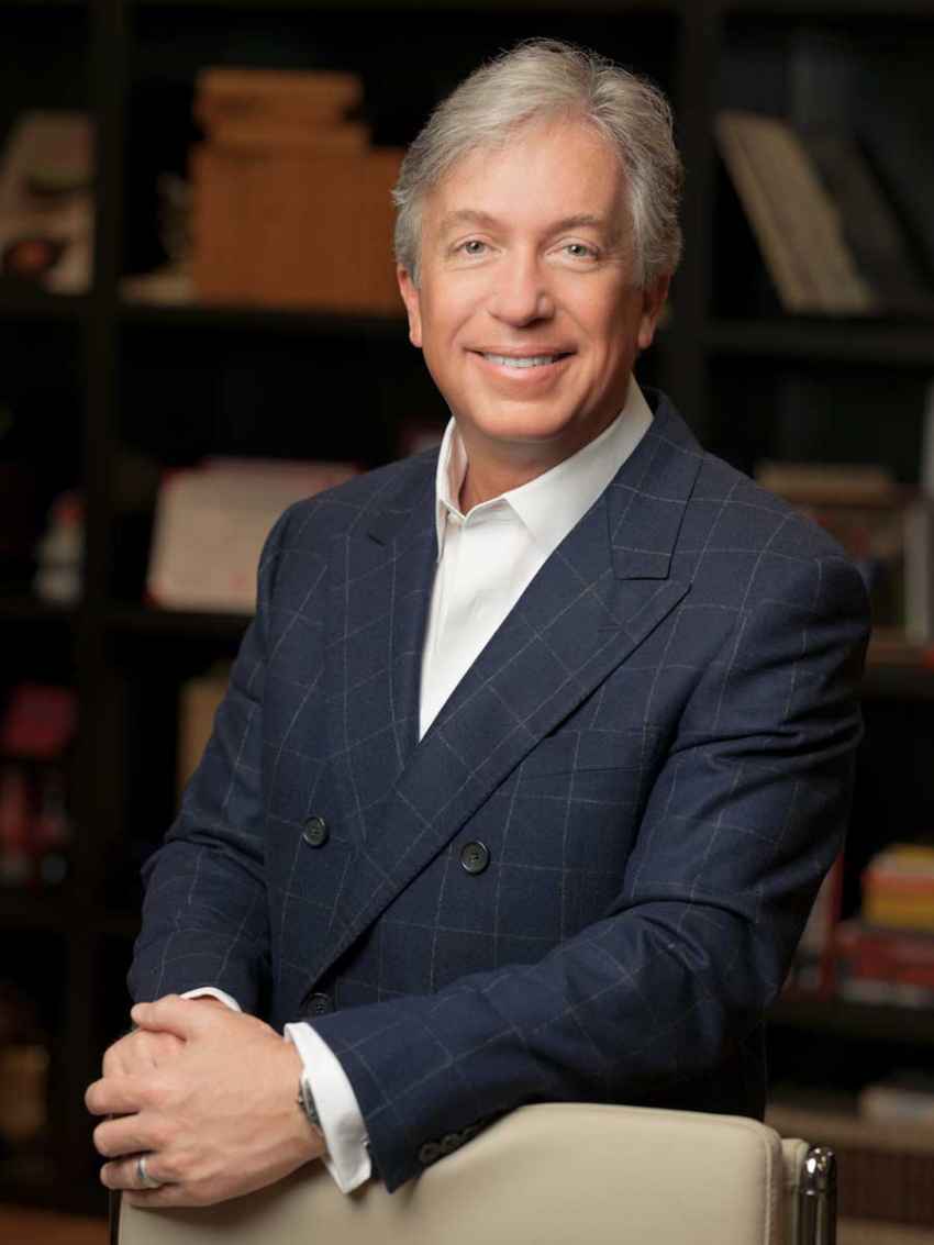 Smiling man in a suit, bookshelf background.